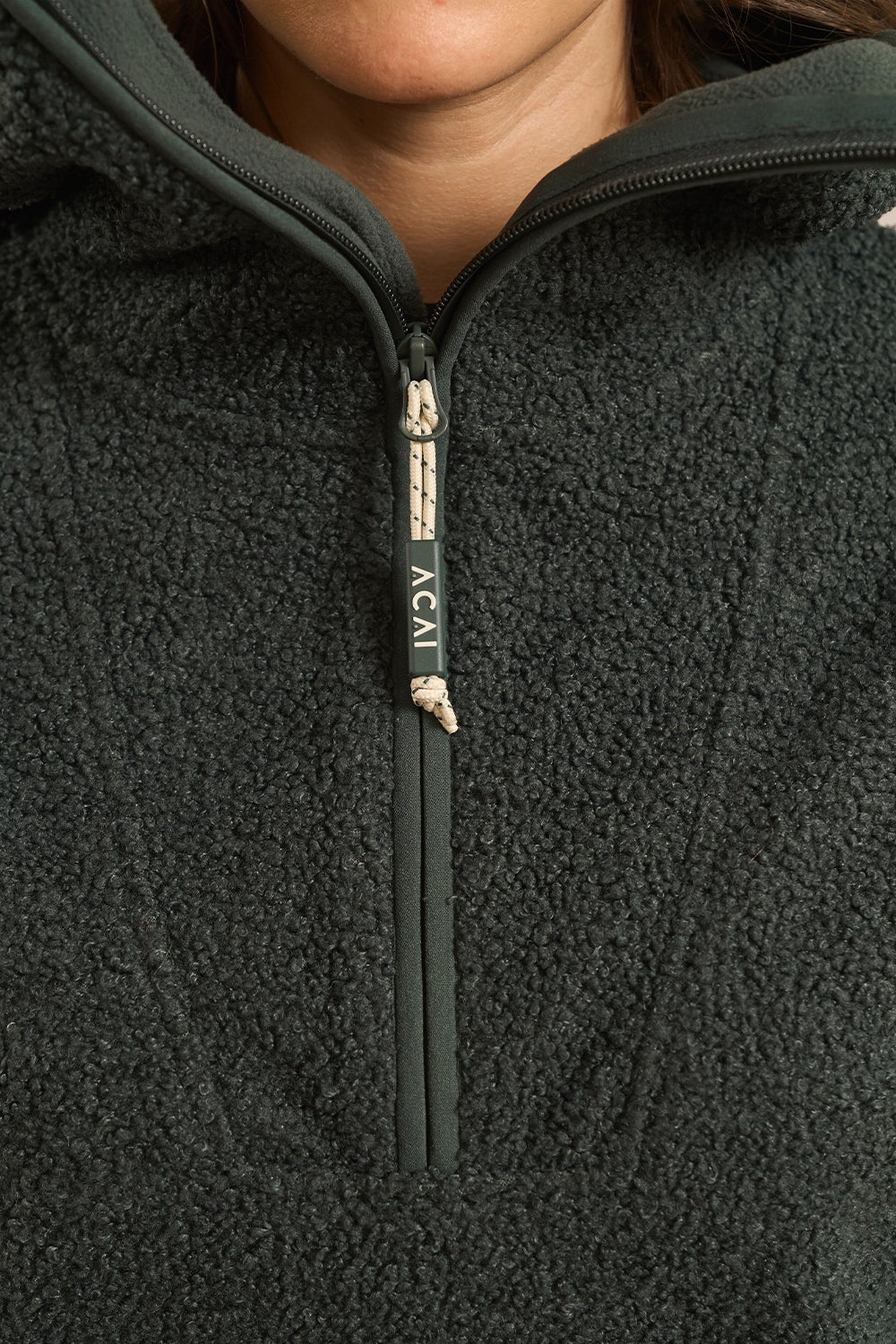 Close-up of a person wearing a forest green fleece quarter-zip pullover with a black zipper pull tab printed with the brand name ACAI.