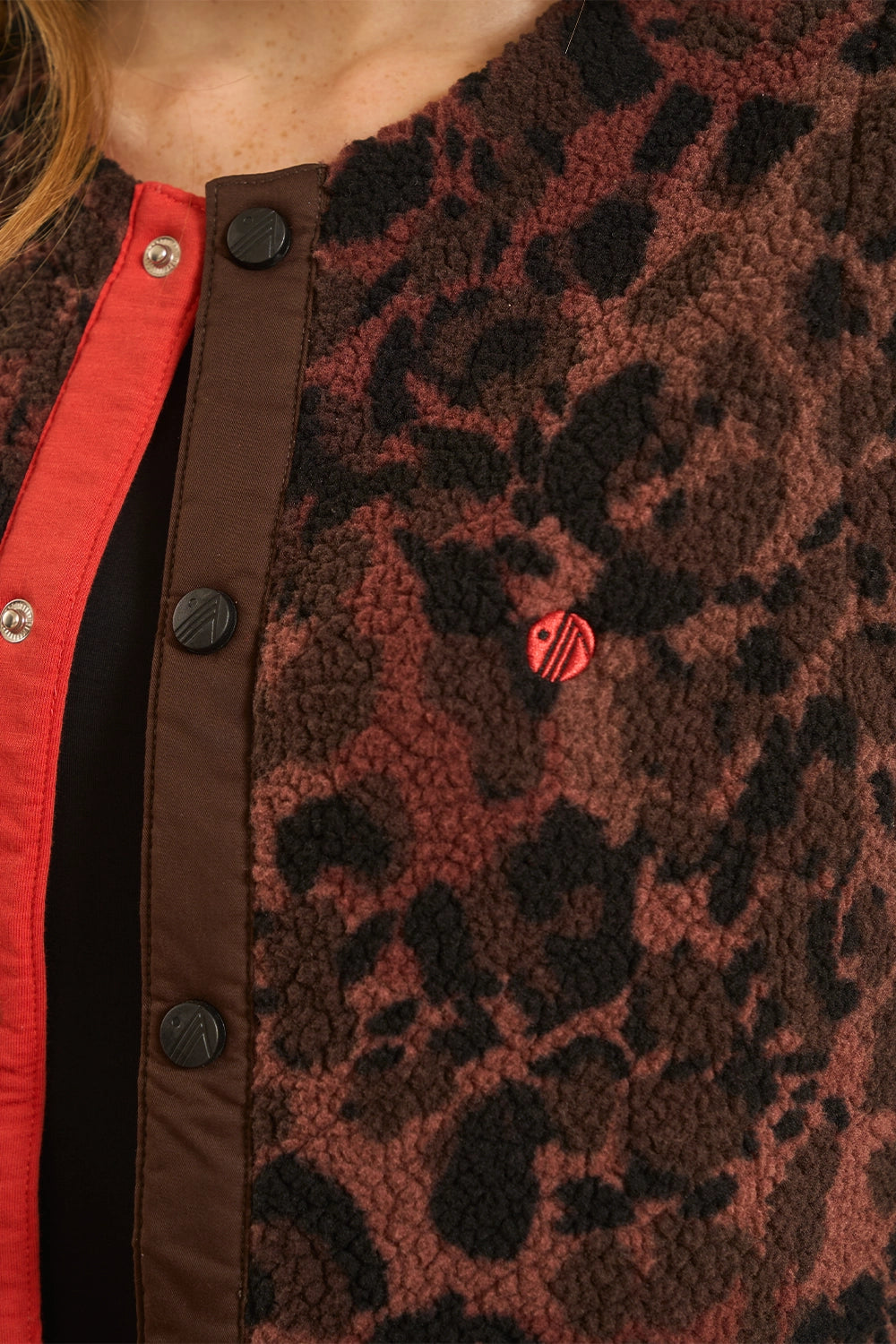 Close-up of a brown and black leopard-print fleece jacket with a red inner lining and snap-button front.