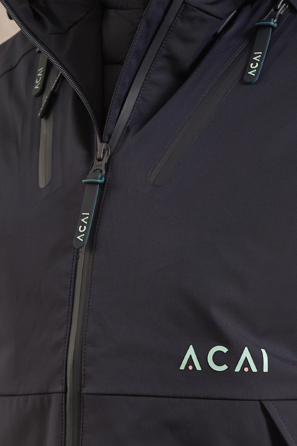 Close-up of a dark navy jacket with a front zipper, zippered pockets, and the Acai logo printed on the lower right chest.