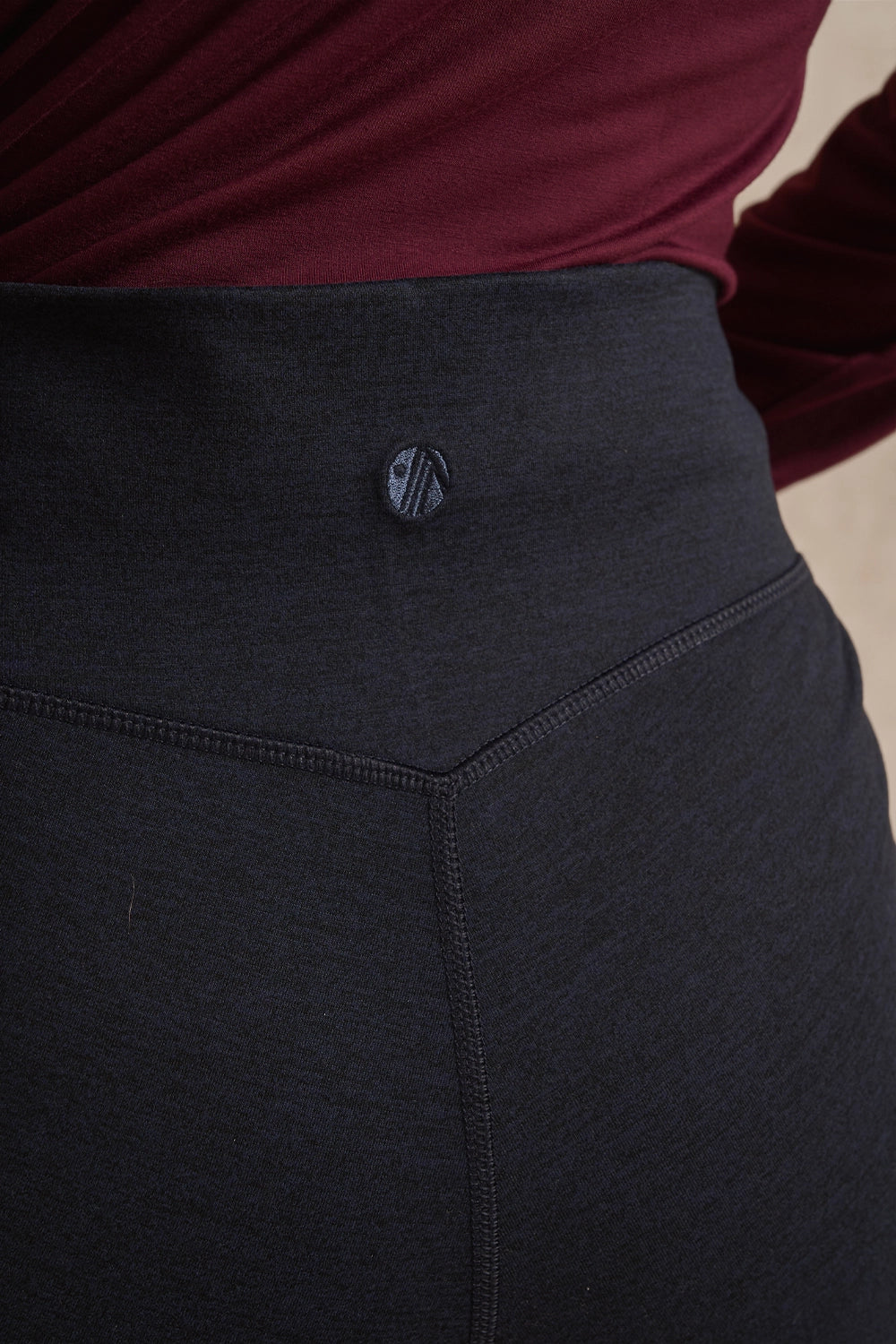 Close-up of a person wearing dark charcoal gray leggings with a small circular logo button at the waistband, paired with a burgundy top.
