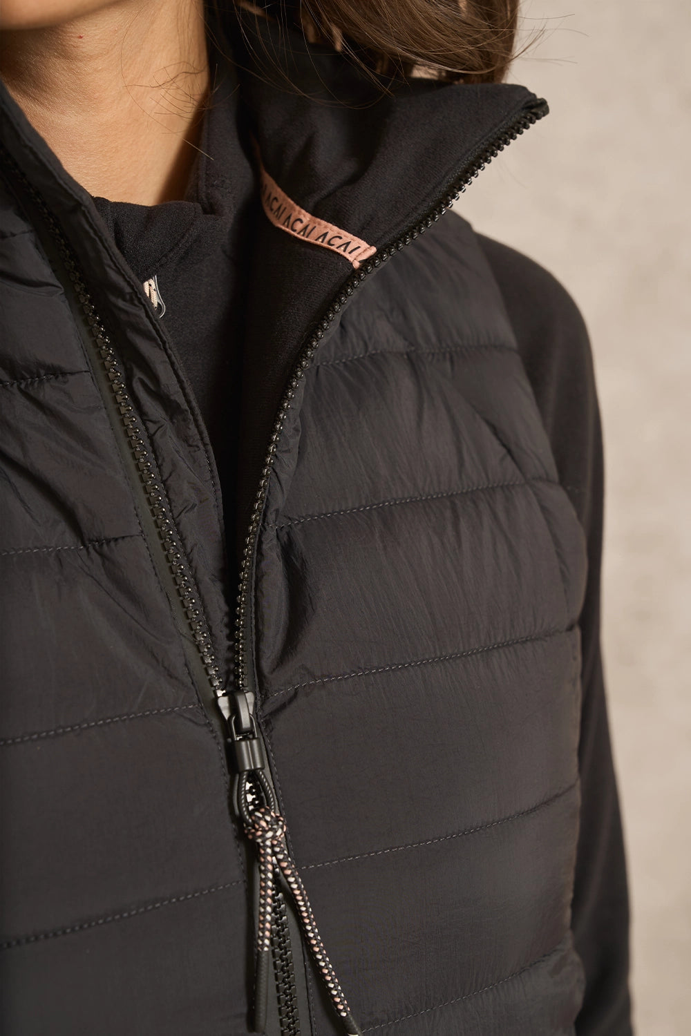 Close-up of a person wearing a black puffer vest with a high collar and a visible Balenciaga brand label on the inner neck.