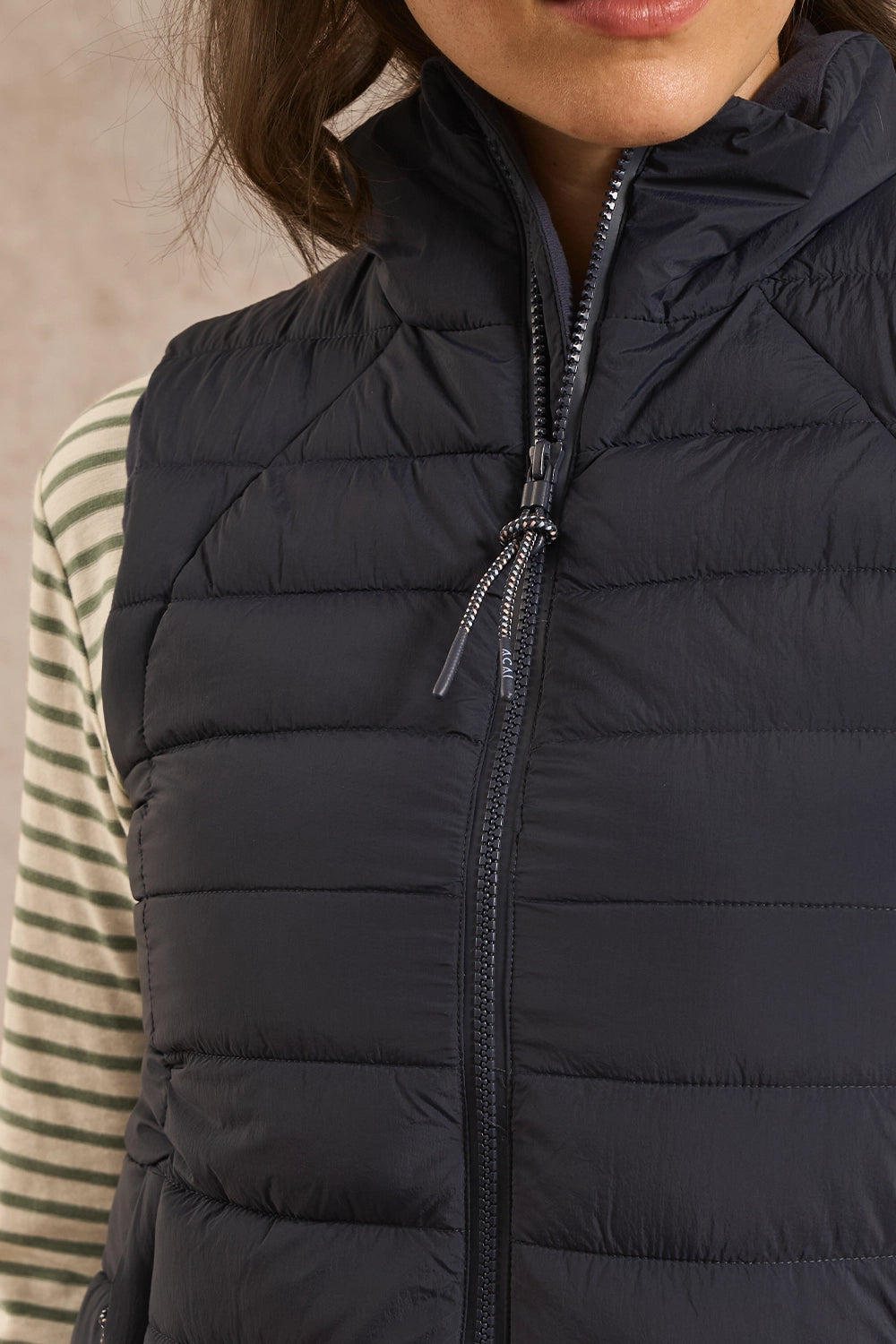 Close-up of a person wearing a dark navy puffer vest over a striped long-sleeve top. The vest has horizontal quilting, a high collar, and a front zipper.