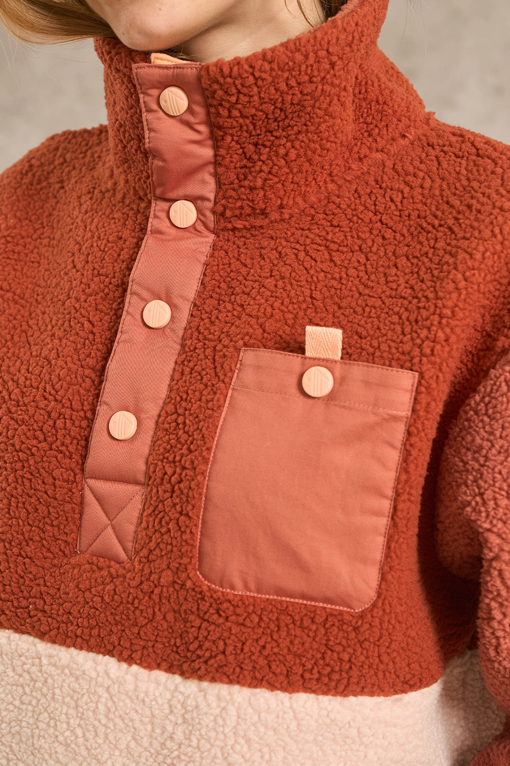 Close-up of a fleece pullover jacket with a high collar, contrasting button placket, and a chest pocket, shown on a model against a neutral background.