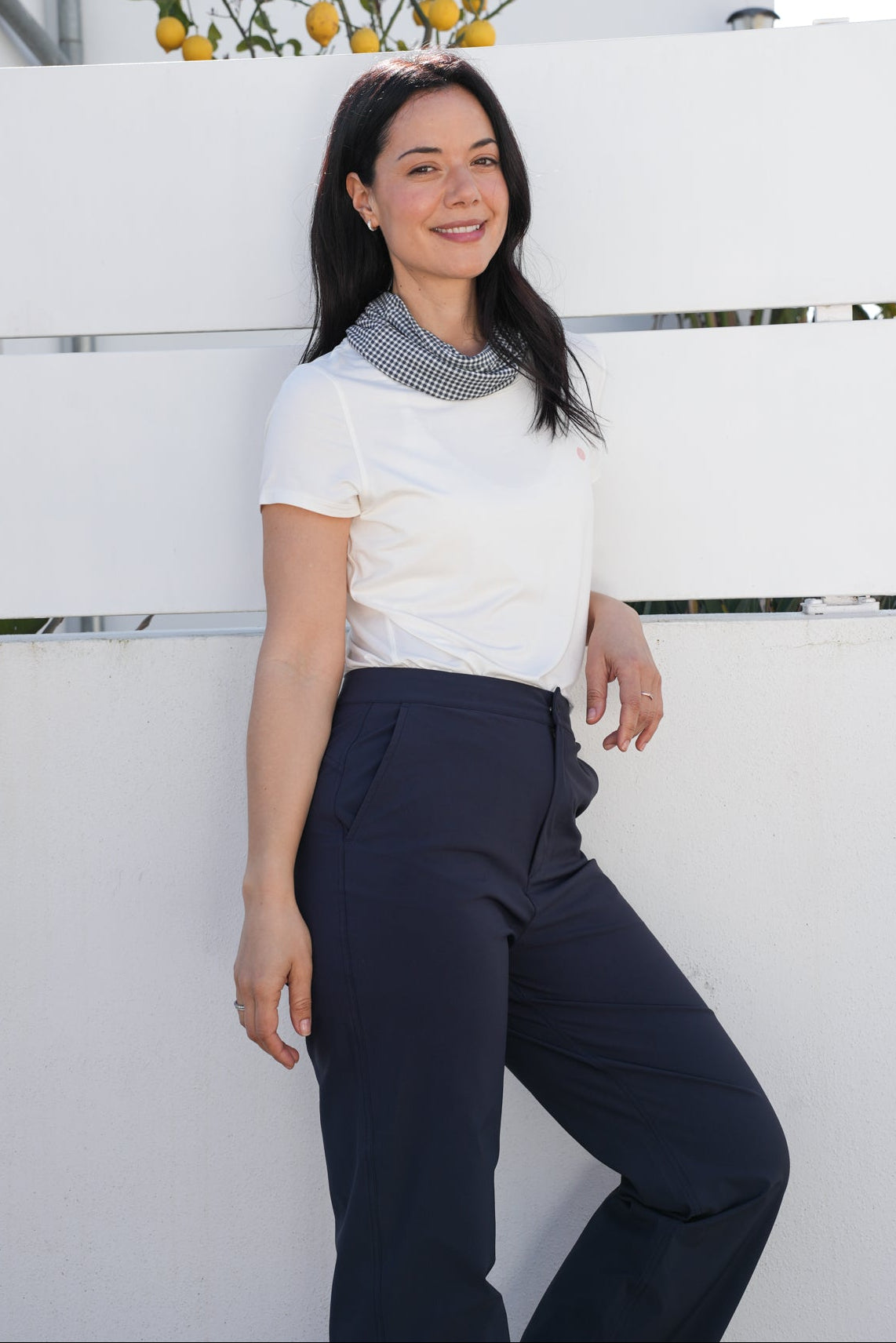 Woman standing against a white wall with a plant in the background