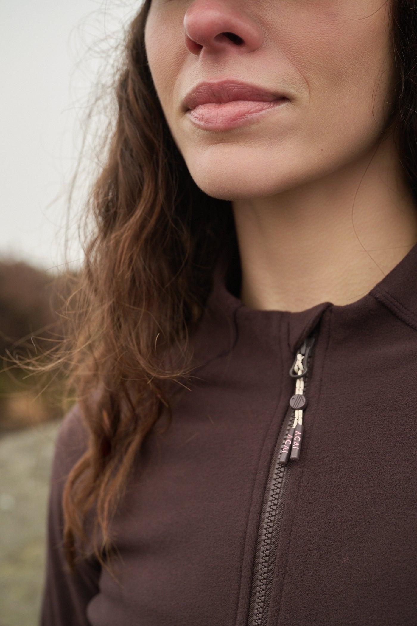 Close-up of a person wearing a brown zip-up hoodie with a blurred natural background