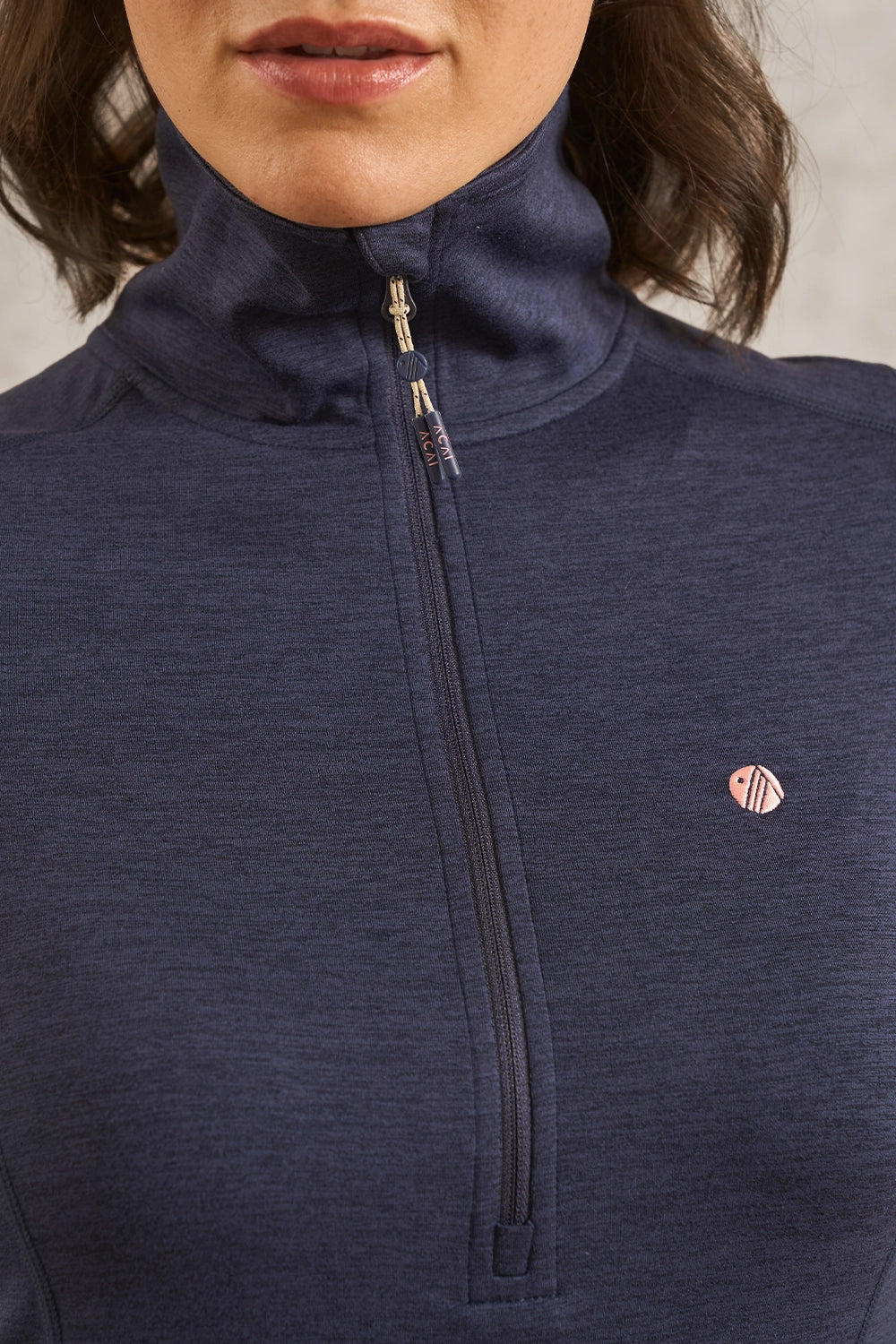 Close-up of a person wearing a navy blue heathered quarter-zip athletic pullover with a small pink and white circular logo on the left chest.