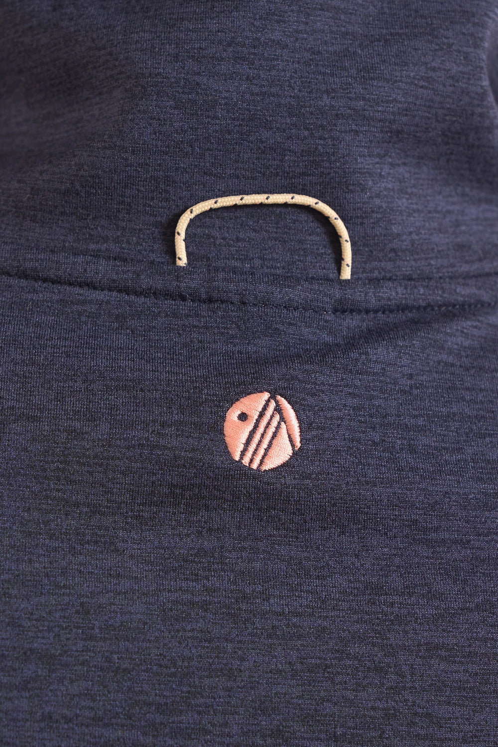 Close-up of a dark navy blue knit garment featuring a small circular embroidered logo in peach and black, with a matching peach embroidered loop detail above it.