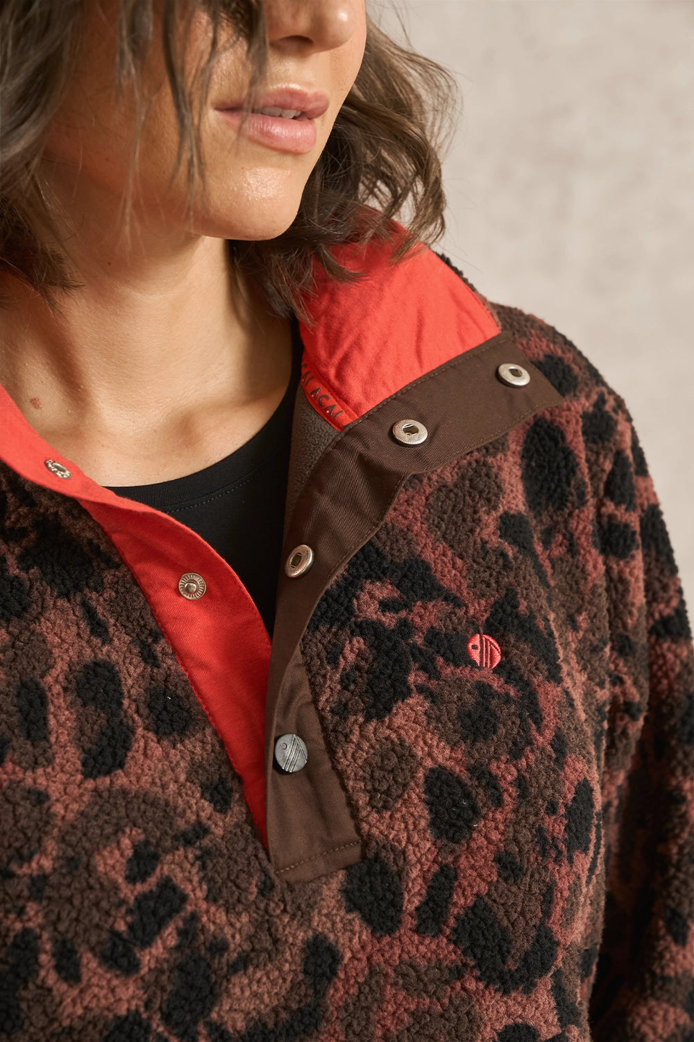 Close-up of a person wearing a brown and black leopard-print fleece pullover with a bright red inner collar and snap-button placket over a black shirt.