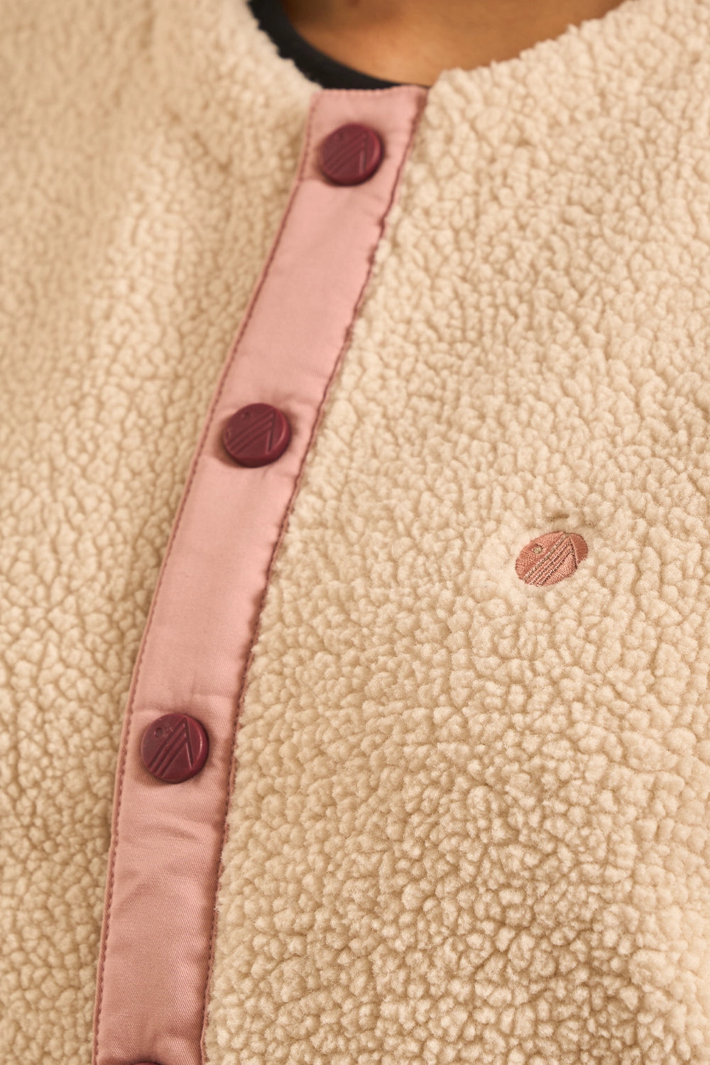 Close-up of a cream sherpa fleece garment with a pink satin trim and dark burgundy buttons down the front.