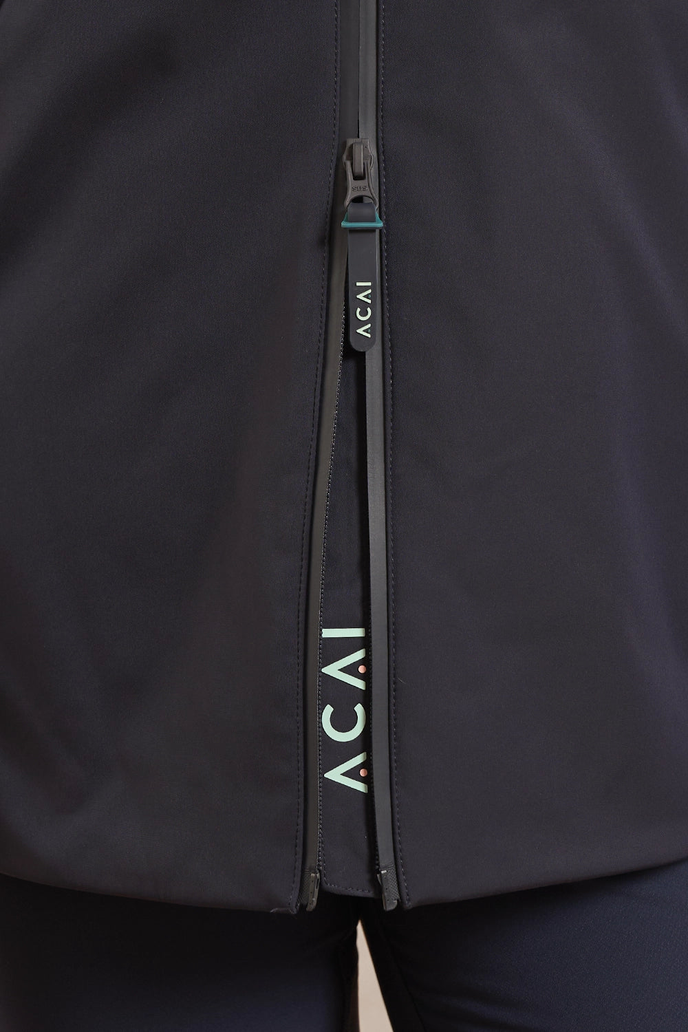 Close-up of a black zippered athletic jacket with the brand name 'ACAI' printed vertically on the zipper pull and along the zipper track.