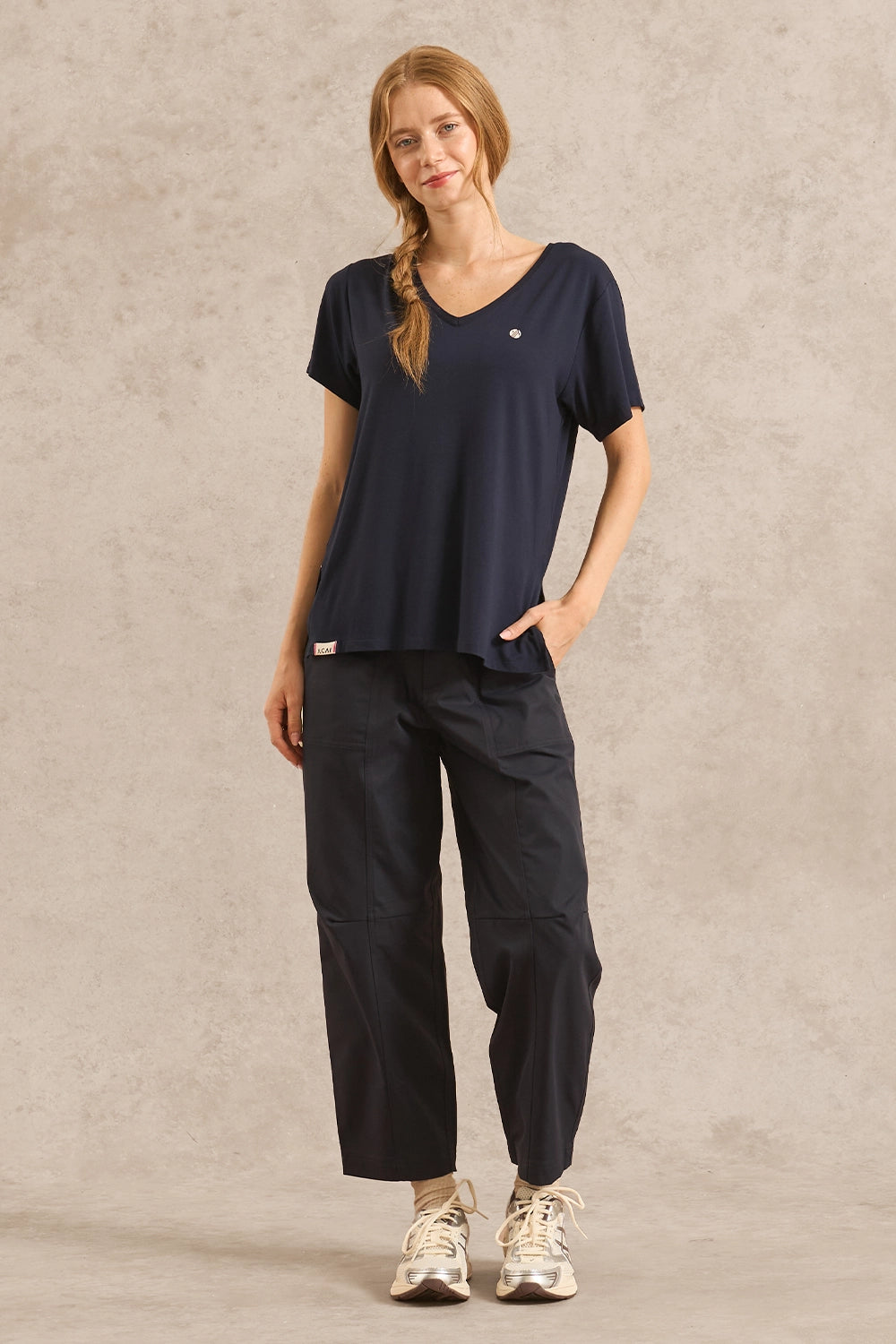 A woman modeling a navy blue short-sleeve V-neck top and matching navy cargo-style pants against a textured beige studio backdrop.